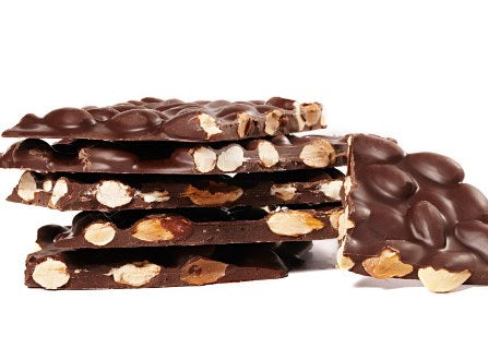 A stack of sugar free dark chocolate almond bark. The thin sheets of bark are broken into pieces, exposing the toasted almonds inside.