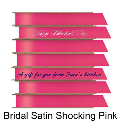 A stack of seven spools of shiny bright pink satin ribbon with custom messages printed on them in different colors. 